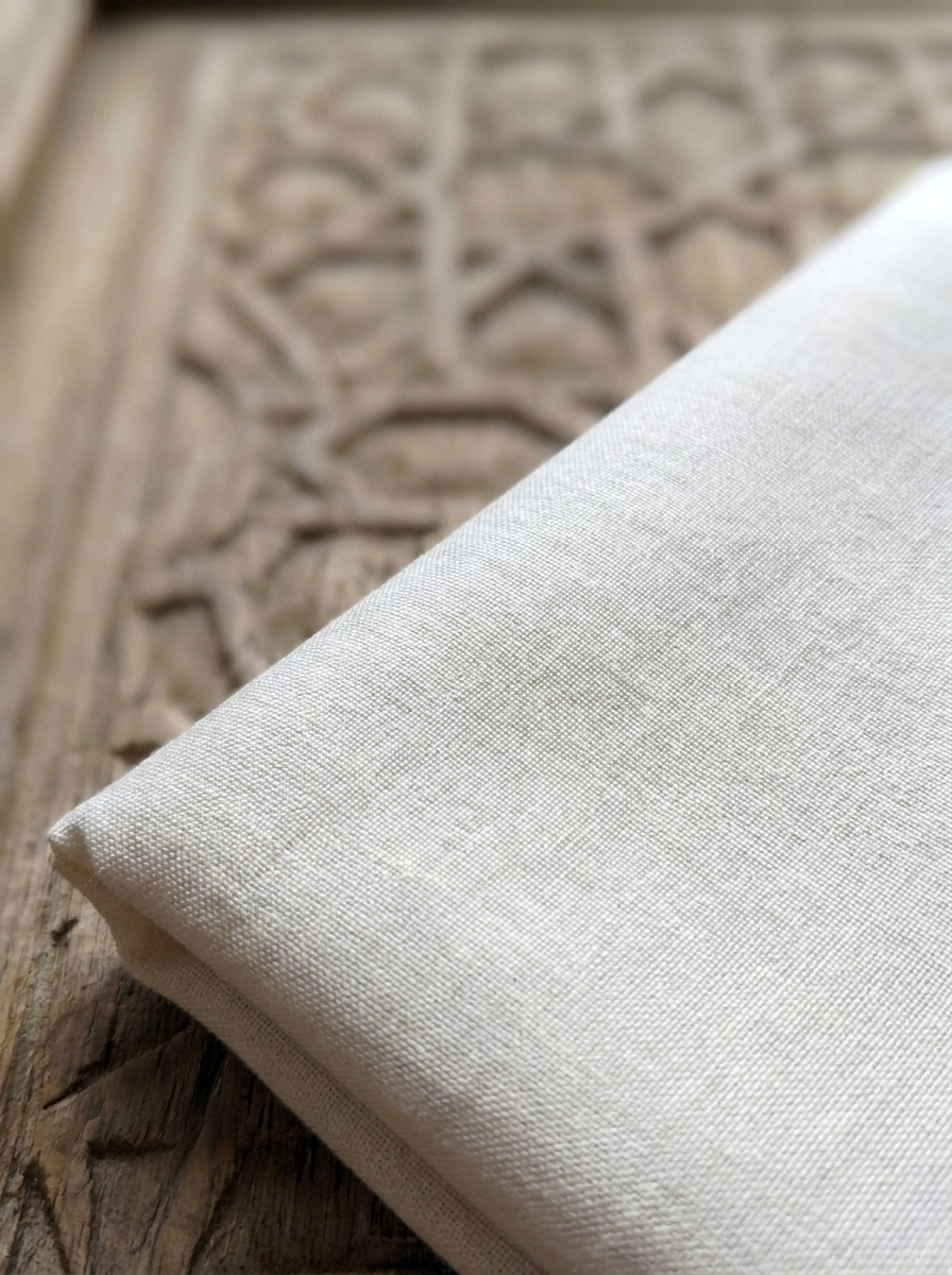 Folded natural cotton kafn cloth resting on carved wood with an Islamic geometric pattern